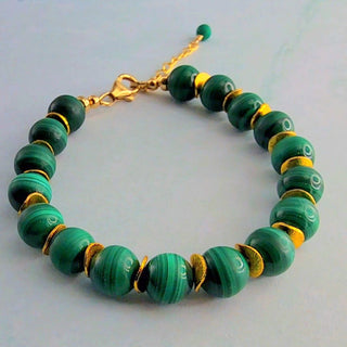 Green beaded bracelet with gold accents on a light blue background